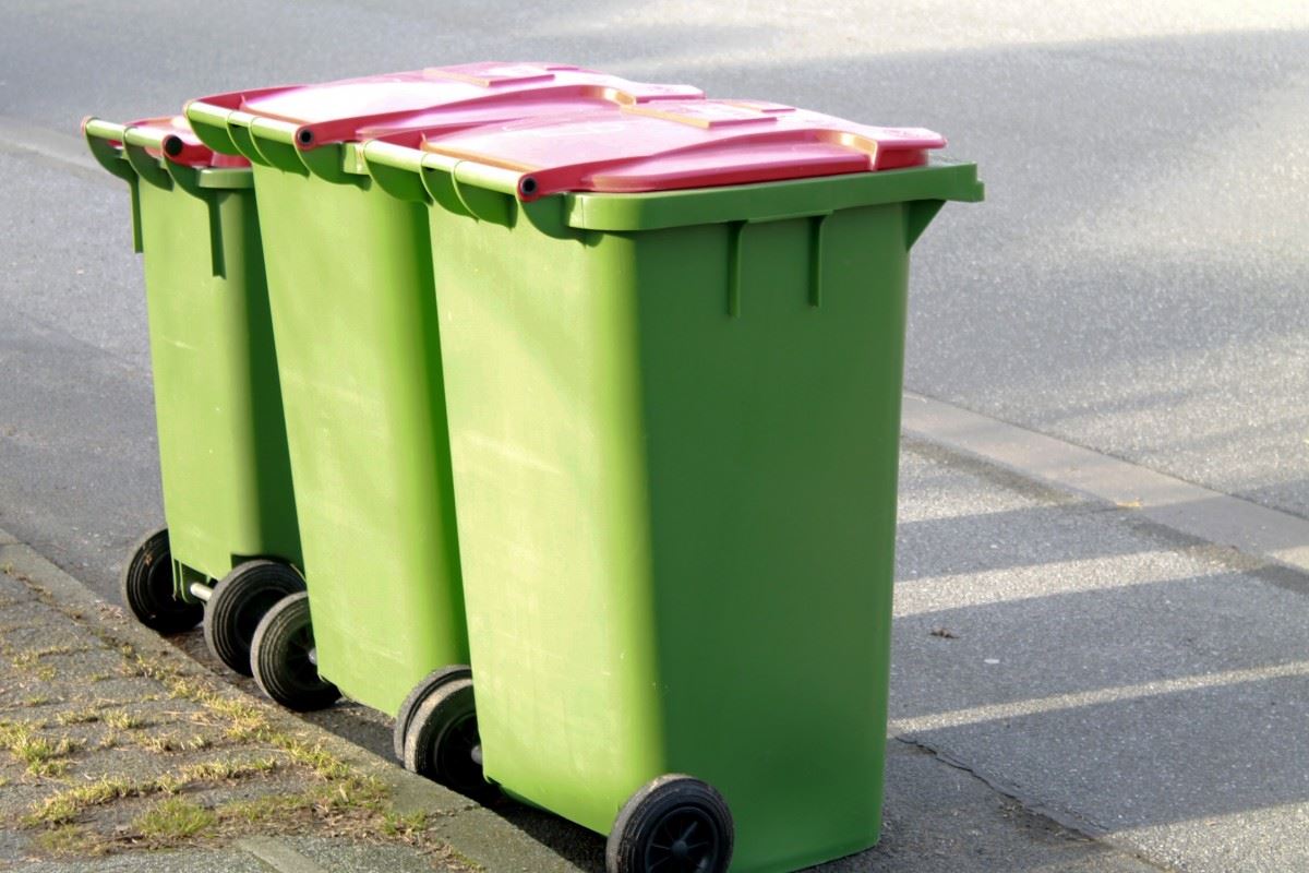 Three green trash bins are lined up on the curb of a street