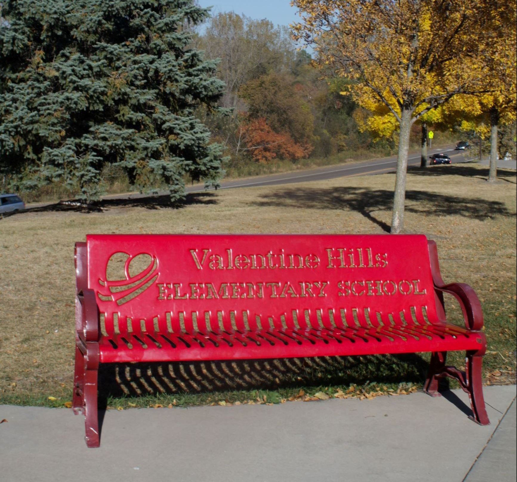 Red metal bench with the words "Valentine Hills Elementary School Bench" on it 